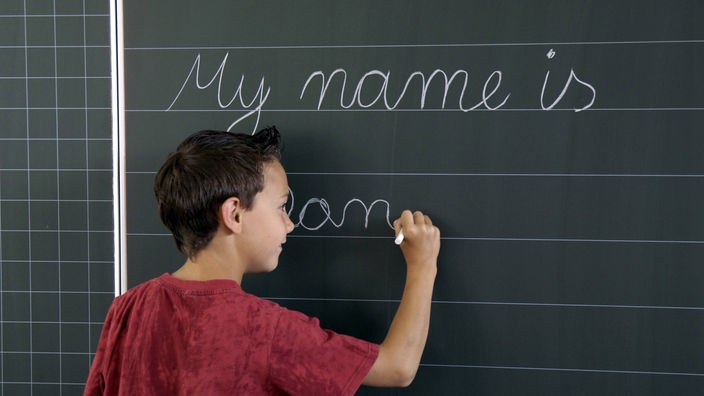 Ein Kind steht vor einer Tafel und schreibt mit Kreide Wörter auf Englisch