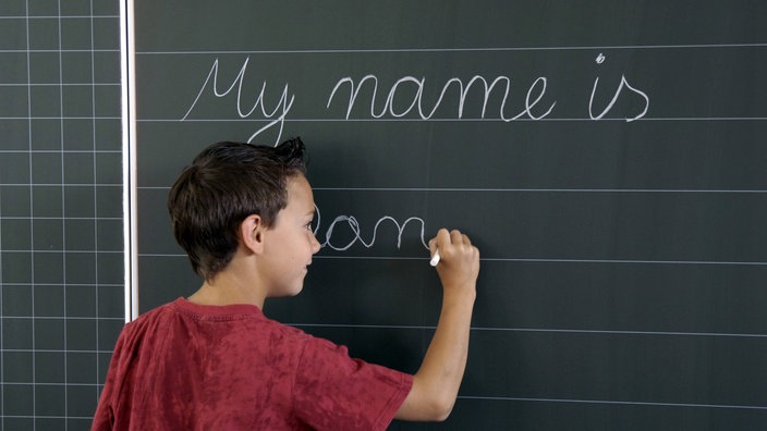 Ein Kind steht vor einer Tafel und schreibt mit Kreide Wörter auf Englisch | Bildquelle: Imago Ein Kind steht vor einer Tafel und schreibt mit Kreide Wörter auf Englisch