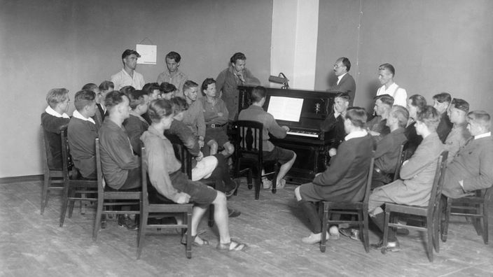 Junge Männer sitzen um ein Klavier 