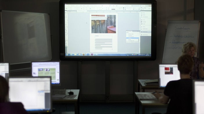 Computerbildschirme und ein Whiteboard in einem abgedunkelten Raum der VHS in Köln