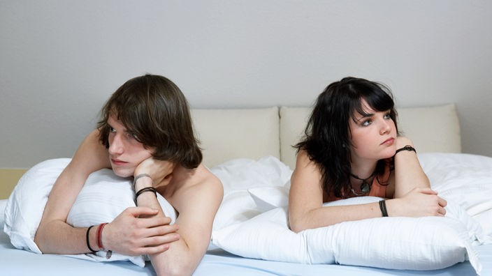 Ein junges Paar liegt bäuchlings auf einem Bett. Beide drehen den Kopf vom anderen weg.