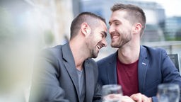 Ein junges Paar in einem Café: die beiden Männer lachen zusammen.