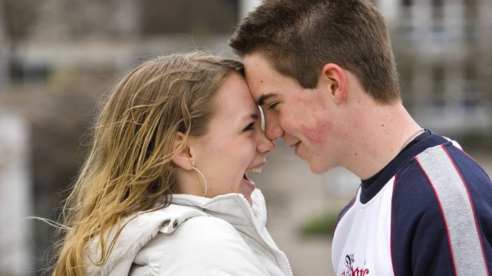 Ein junges Paar hat die Stirnen zusammengelegt und schaut sich lächelnd in die Augen.