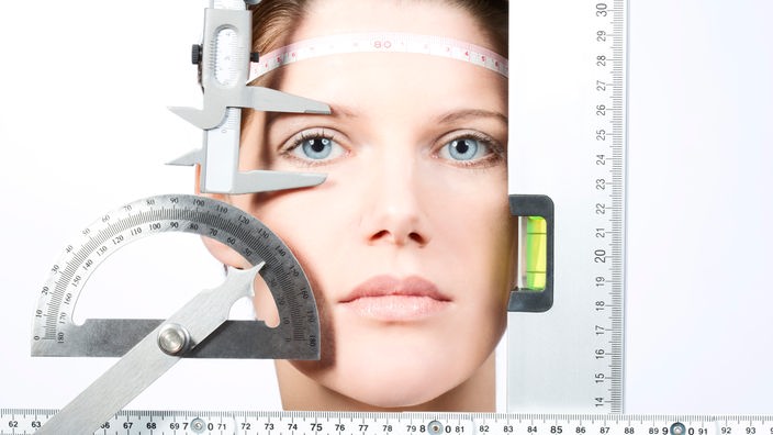 Symbolbild: Das Gesicht einer Frau wird mit mehreren geometrischen Instrumenten vermessen