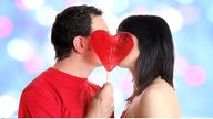 Ein Paar küsst sich hinter einem Herzlolli.