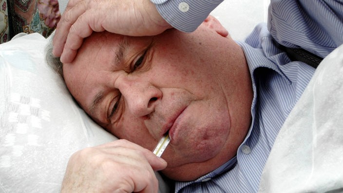 Älterer Mann liegt mit Fieberthermometer im Mund im Bett 