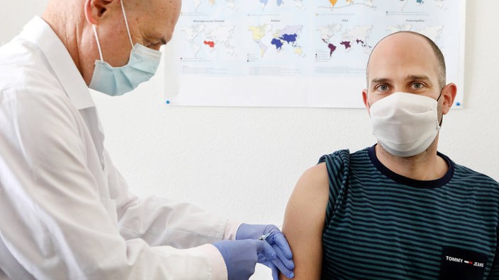 Ein Arzt im weißen Kittel mit Mundschutz impft einen anderen Mann