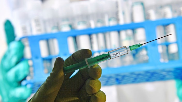 Eine Hand mit Gummihandschuh hält eine Einwegspritze mit Impfstoff