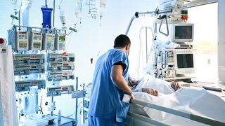 Ein Pfleger beugt sich über einen Patienten, der in einem Krankenbett liegt