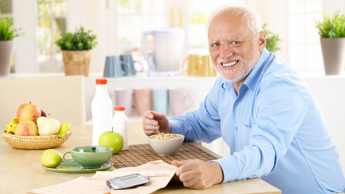Älterer Mann sitzt am Frühstückstisch und isst Müsli