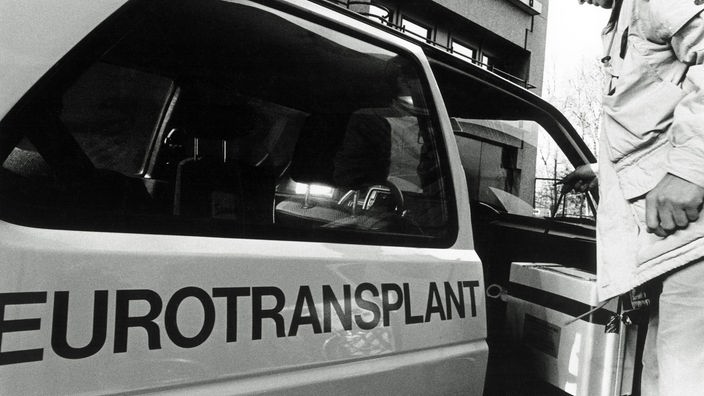 Mann stellt eine Box mit einem Spenderorgan in ein Auto mit der Aufschrift "Eurotransplant"