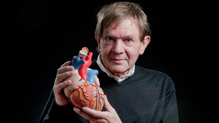 Ein transplantierter Mann hält das Modell eines Herzens in die Kamera
