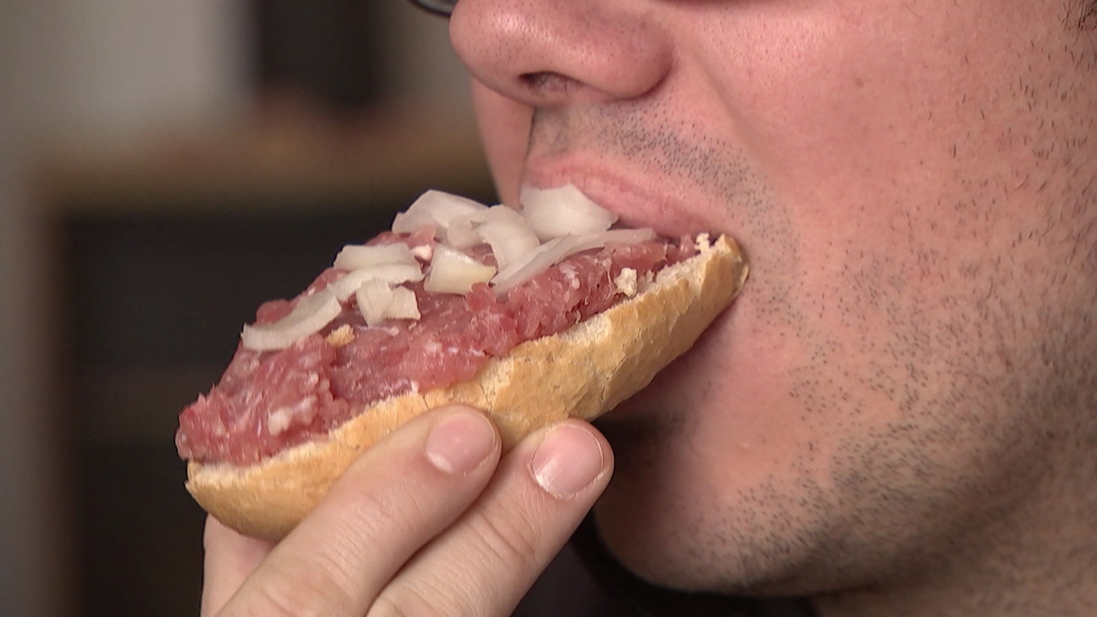 Ein Mann beißt in ein Mettbrötchen.