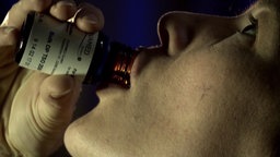 Eine Person trinkt aus einem Arzneifläschchen.