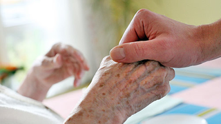 Pfleger hält die Hand einer alten Frau.