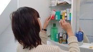 Eine Frau nimmt Arzneimittel aus ihrem Medikamentenschrank.