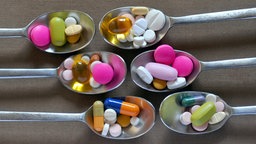 Verschiedene Tabletten und Kapseln auf Silberlöffeln.