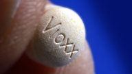Zwei Finger halten eine VIOXX-Tablette.