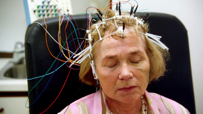 Am Kopf einer älteren Frau sind mehrere Elektroden mit Kabeln angeschlossen.
