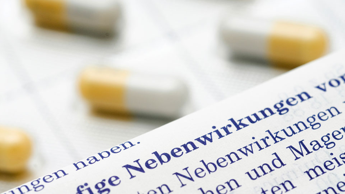 Nahaufnahme eines Beipackzettels mit dem Wort "Nebenwirkung" im Vordergrund und dahinter gelb-weiße Kapseln. | Bildquelle: Mauritius Nahaufnahme eines Beipackzettels mit dem Wort "Nebenwirkung" im Vordergrund und dahinter gelb-weiße Kapseln.