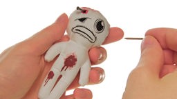 Voodoo-Puppe in der linken Hand einer Frau; in der rechten Hand hält sie einen Nagel.
