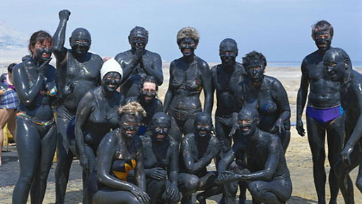 Eine Menschengruppe ist mit schwarzem Heilschlamm aus dem Toten Meer eingerieben.