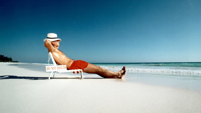 Ein Mann sitzt im Liegestuhl am Strand in der Sonne