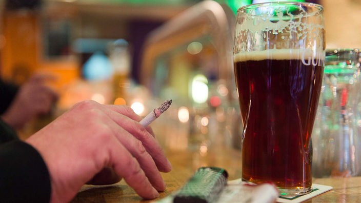 Eine Hand mit Zigarette zwischen den Fingern, daneben steht ein Bierglas.