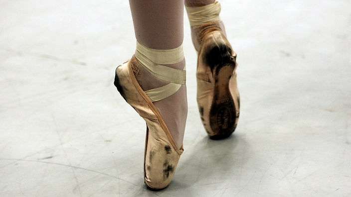 Nahaufnahme von Füßen in goldenen Ballettschuhen.