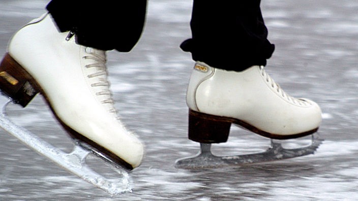 Nahaufnahme von weißen Schlittschuhen, die übers Eis gleiten.