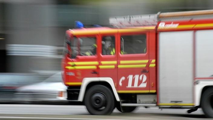 Ein rotes Feuerwehrfahrzeug mit der Rufnummernaufschrift 112 kommt von rechts. Es ist durch die Fahrgeschwindigkeit nur unscharf zu erkennen.