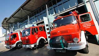 Drei rote Feuerwehrfahrzeuge stehen einsatzbereit vor den geöffneten Toren des Feuerwehrgebäudes