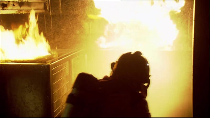 Feuerwehrmann in Schutzkleidung in einem Raum mit offenen Flammen.