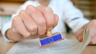 Hand mit einem EU-Stempel in der Hand über Unterlagen.