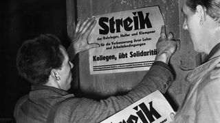Zwei Männer kleben Plakate mit einem Streik-Aufruf an eine Wand