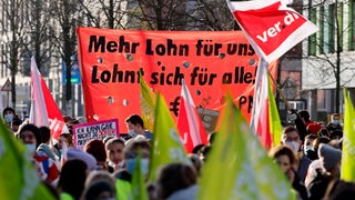 Bei einer Demonstration steht auf einem roten Transparent "Mehr Lohn für uns lohnt sich für alle"
