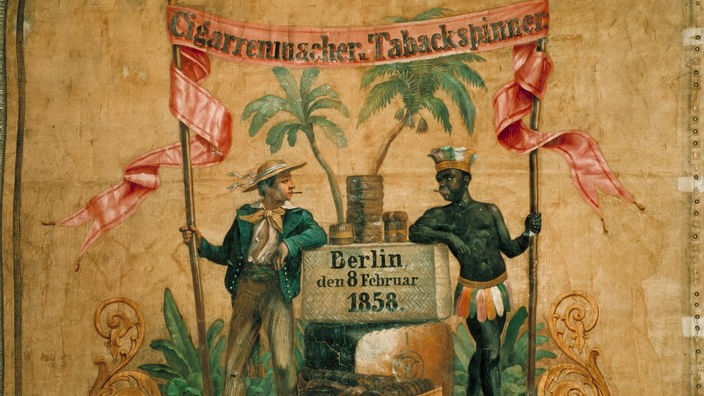 Auf einer alten Fahne stehen ein weißer und ein schwarzer Zigarrenarbeiter neben Zigarrenkisten