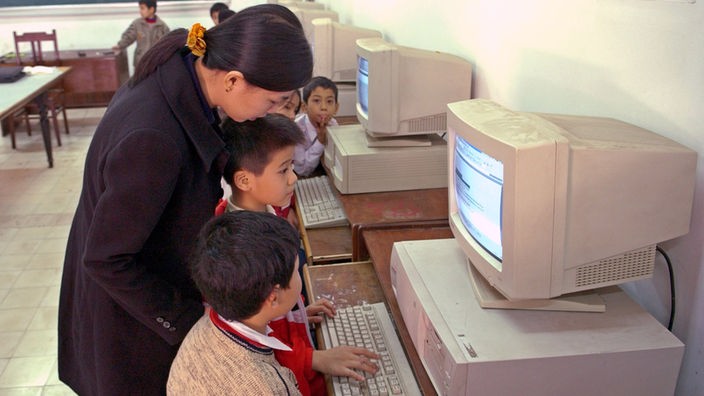 Eine Frau hilft Kindern am Computer in Vietnam