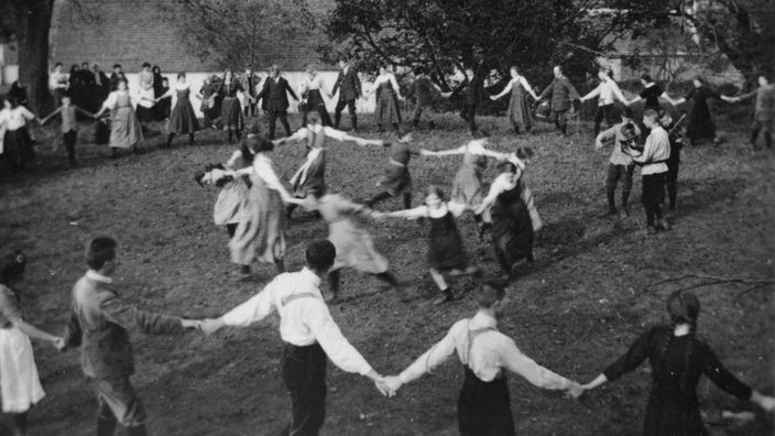 Historische Aufnahme einer Wandervogelgruppe, die in zwei Reihen im Ringelreihen tanzt
