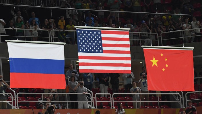 Die Nationalflaggen der 3 Großmächte Russland, USA und China werden bei einem Sportereignis nebeneinander gehisst.