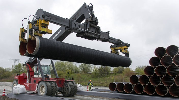 Ein Kranfahrzeug mit zwei Rohren einer Erdgas-Pipeline an einer Baustelle.
