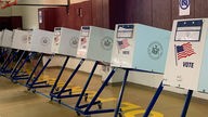 Amerikanische Wahlurnen stehen nebeneinander aufgereiht in einer Turnhalle.