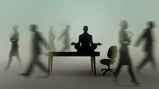 Ein Geschäftsmann sitzt meditierend auf seinem Schreibtisch, während seine Kollegen hektisch um ihn herumlaufen