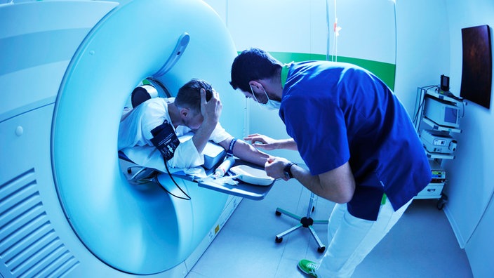 Patient im Computertomographen wird von Arzt behandelt. | Bildquelle: dpa Patient im Computertomographen wird von Arzt behandelt.