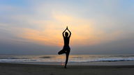 Eine Frau macht in der Dämmerung Yoga am Strand.