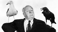 Der Regisseur Alfred Hitchcock posiert mit einer Möwe und einem Raben auf seinen Schultern.