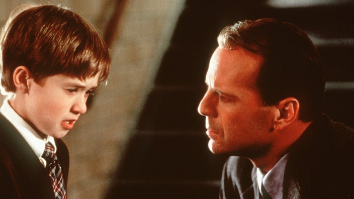 Schauspieler Bruce Willis als Therapeut hört aufmerksam seinem Patienten zu, einem Jungen (Haley Joel Osment), der Tote sieht.