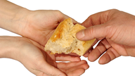 Zwei offene Hände halten ein Stück Brot, nachdem eine weitere Hand greift.