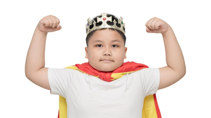 Moppeliger Junge mit Krone zeigt seine Muskeln.