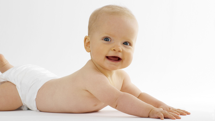 Baby liegt auf dem Bauch und lächelt in die Kamera.